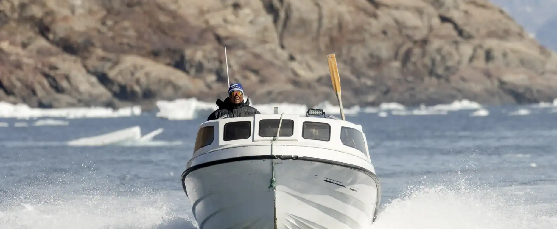 Boat navigating through the icy waters of East Greenland with mountains and icebergs in the background.