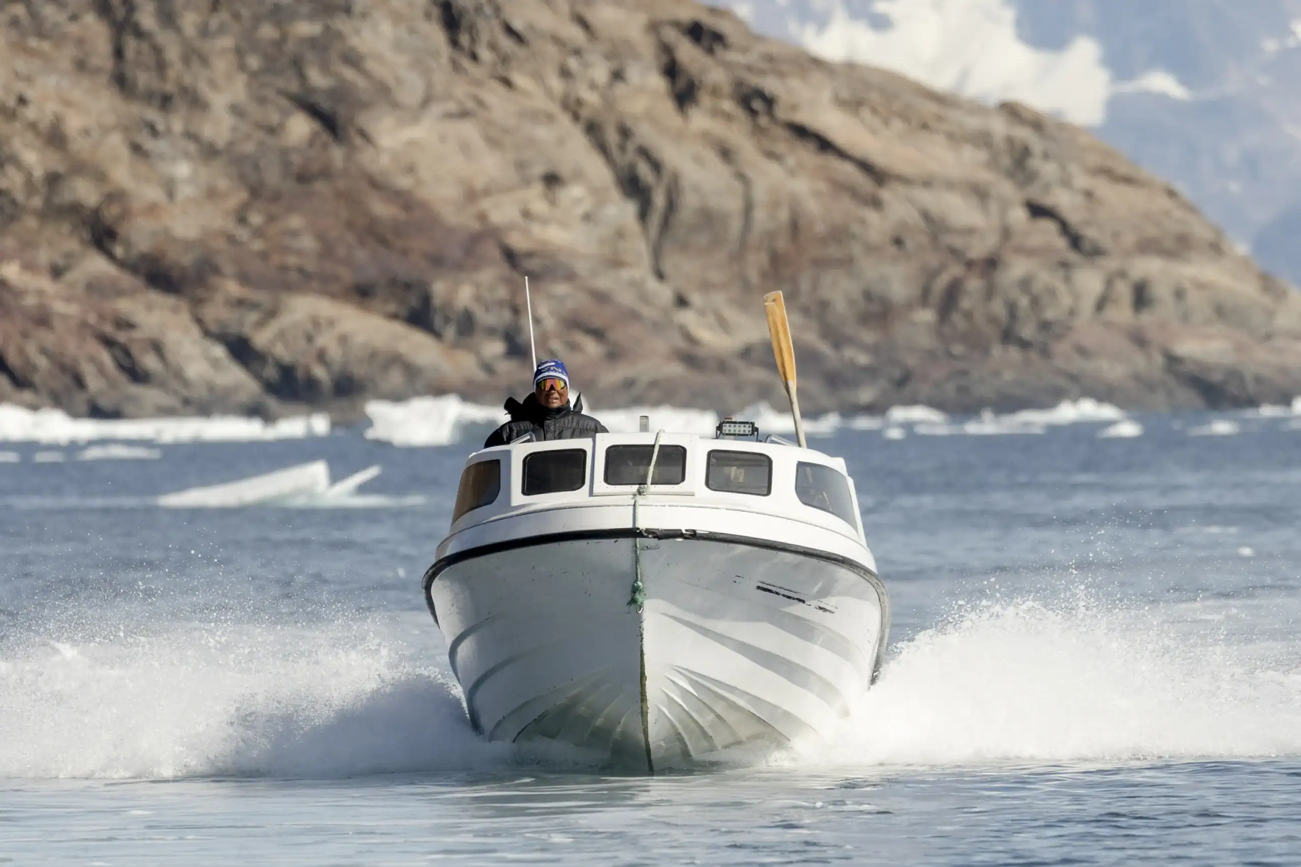Boat navigating through the icy waters of East Greenland with mountains and icebergs in the background.