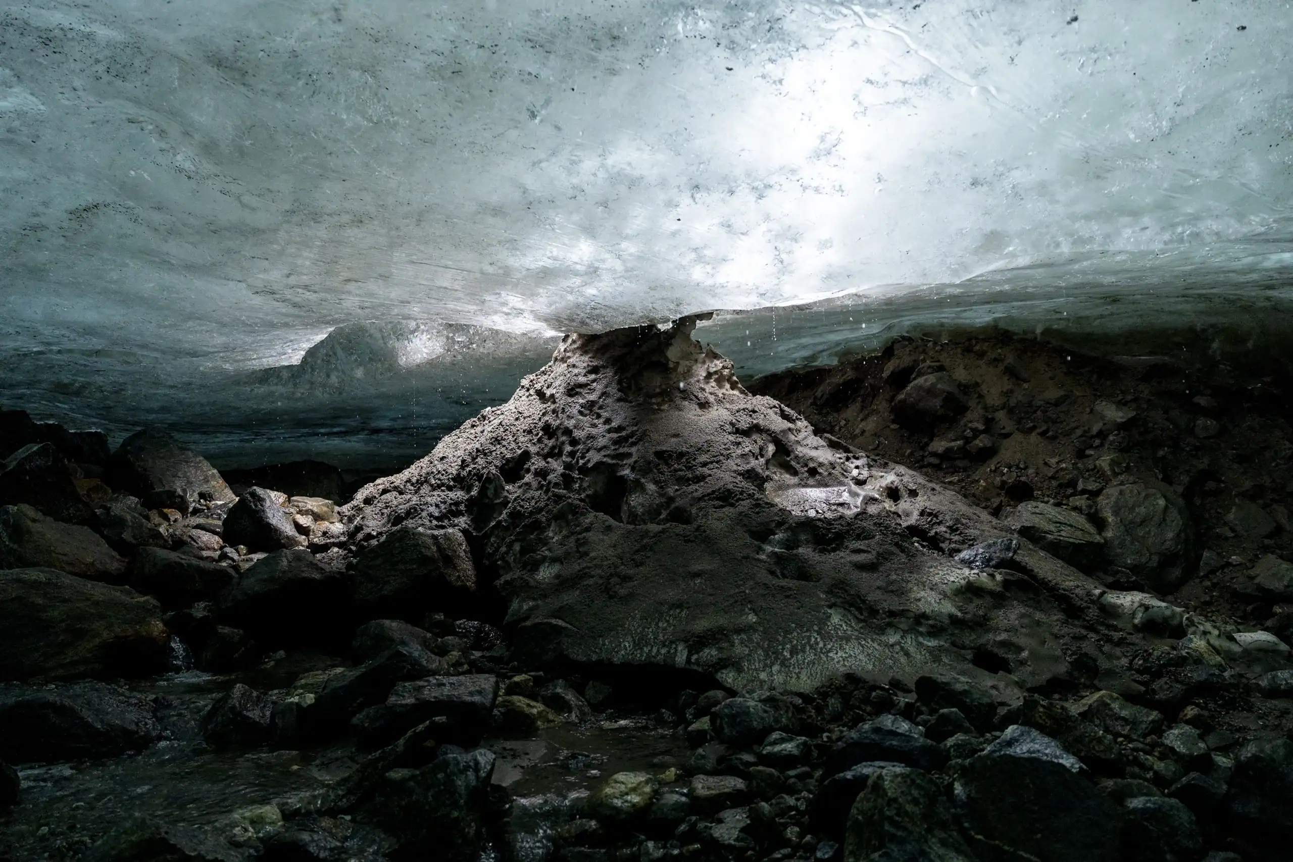 View from inside a subglacial cavern in East Greenland, with an icy ceiling and rocky ground below.