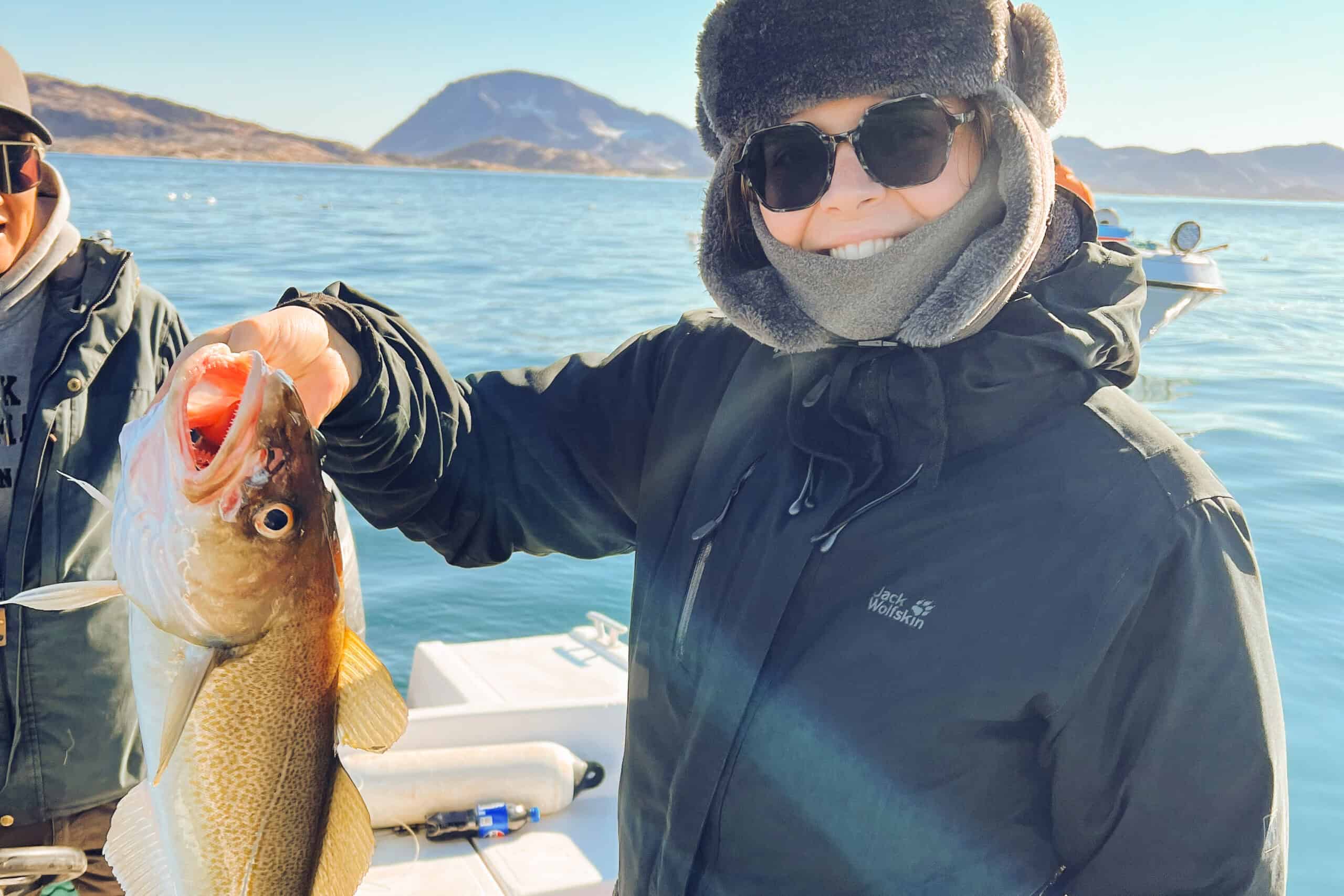 Tourist catching a fish on a boat in Tasiilaq's fjord.