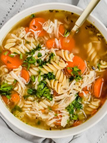 This is a photo of the healthy instant pot chicken noodle soup in a bowl topped with parsley and a golden spoon in the bowl.