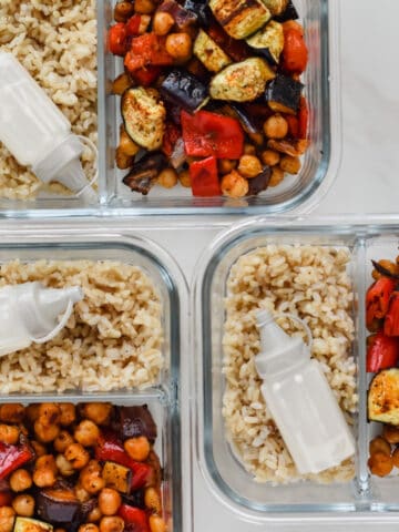 This is a photo of the vegan mediterranean sheet pan meal prep in 3 different meal prep containers. Each has a portion of the recipe along with some brown rice and the tahini dressing.