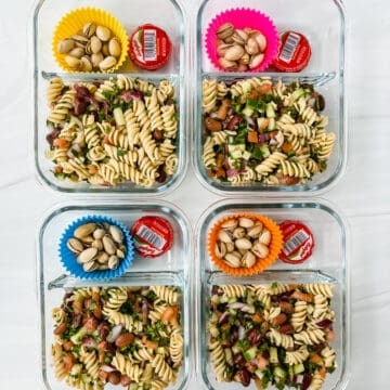 This is a photo of the no mayo pasta salad meal prep in a bento box glass 2 compartment container with pistachios in a silicone tin muffin liner and baby bel cheese for more protein