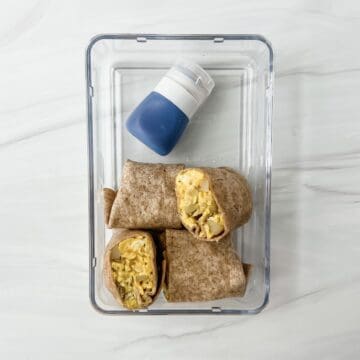 This is a photo of the 2 tex-mex breakfast burritos in a clear container with salsa in a small container.