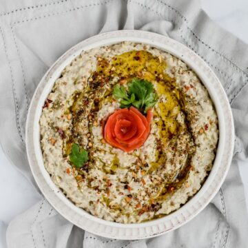 an overhead shot of the baba ganoush eggplant dip topped with olive oil. spices and a tomato flower in the center.