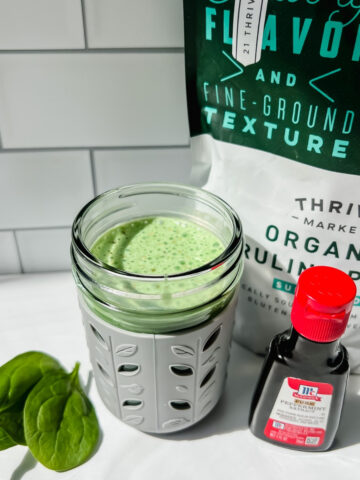 This is a photo of the healthy shamrock shake that's toddler and kid friendly in a small toddler sippy cup with the spirulina powder, spinach and peppermint extract on the side.