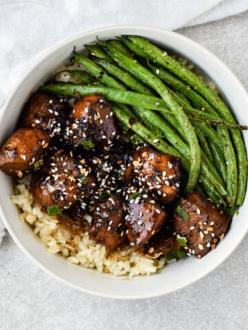 this is a photo of the dairy-free honey garlic chicken on a bed of rice and green beans in a bowl with a kitchen towel.