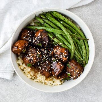 this is a photo of the dairy-free honey garlic chicken on a bed of rice and green beans in a bowl with a kitchen towel.