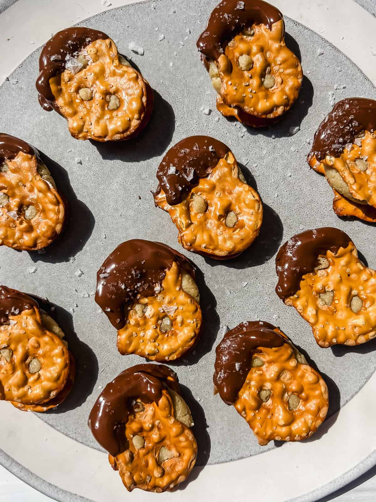 This is a top view of my healthy dairy-free peanut butter pretzel bites that are a delightful fusion of salty and sweet flavors and make for a delicious dessert.They are on a plate and chocolate dipped toped with maldon sea salt. 