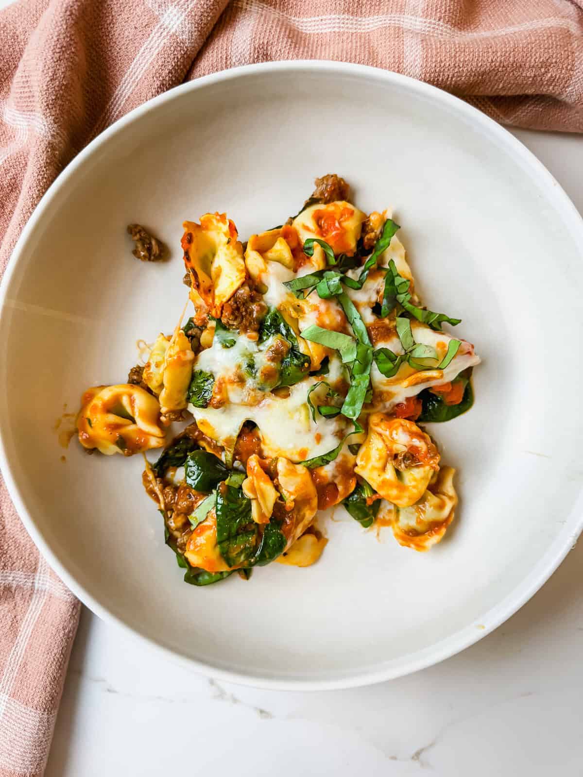 close up of my tortellini casserole in a plate with fresh basil on top. 