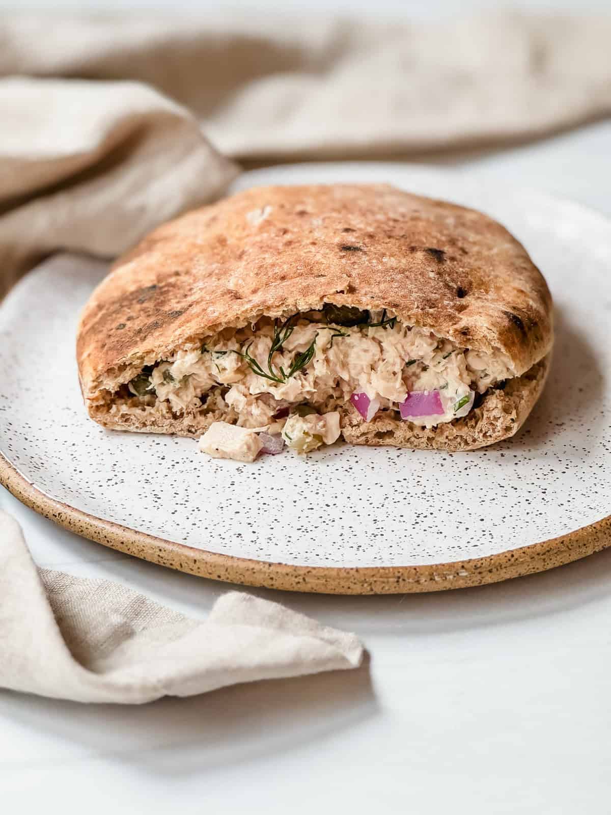 this is a side view of my caper tuna salad, stuffed into a whole wheat pita on a plate. 