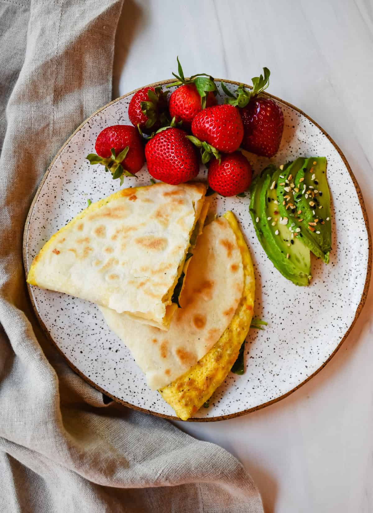 This is a top view of my one pan breakfast quesadillas cut in half and served with avocado slices and fresh strawberries on a plate.