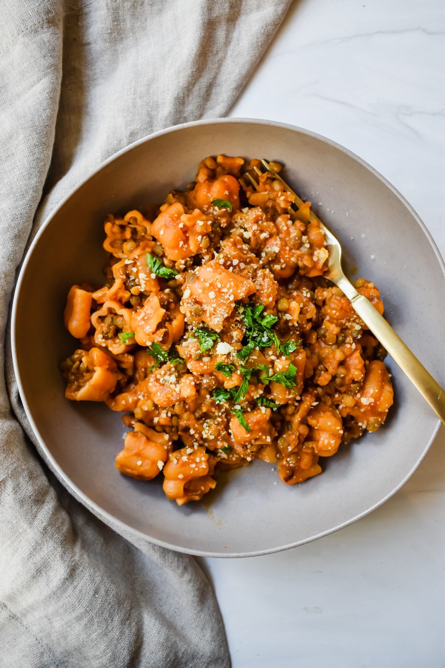 this is a top view of my lentil ragu in a bowl with a gold fork. it is also garnished with fresh parsley and grated parmesan. 