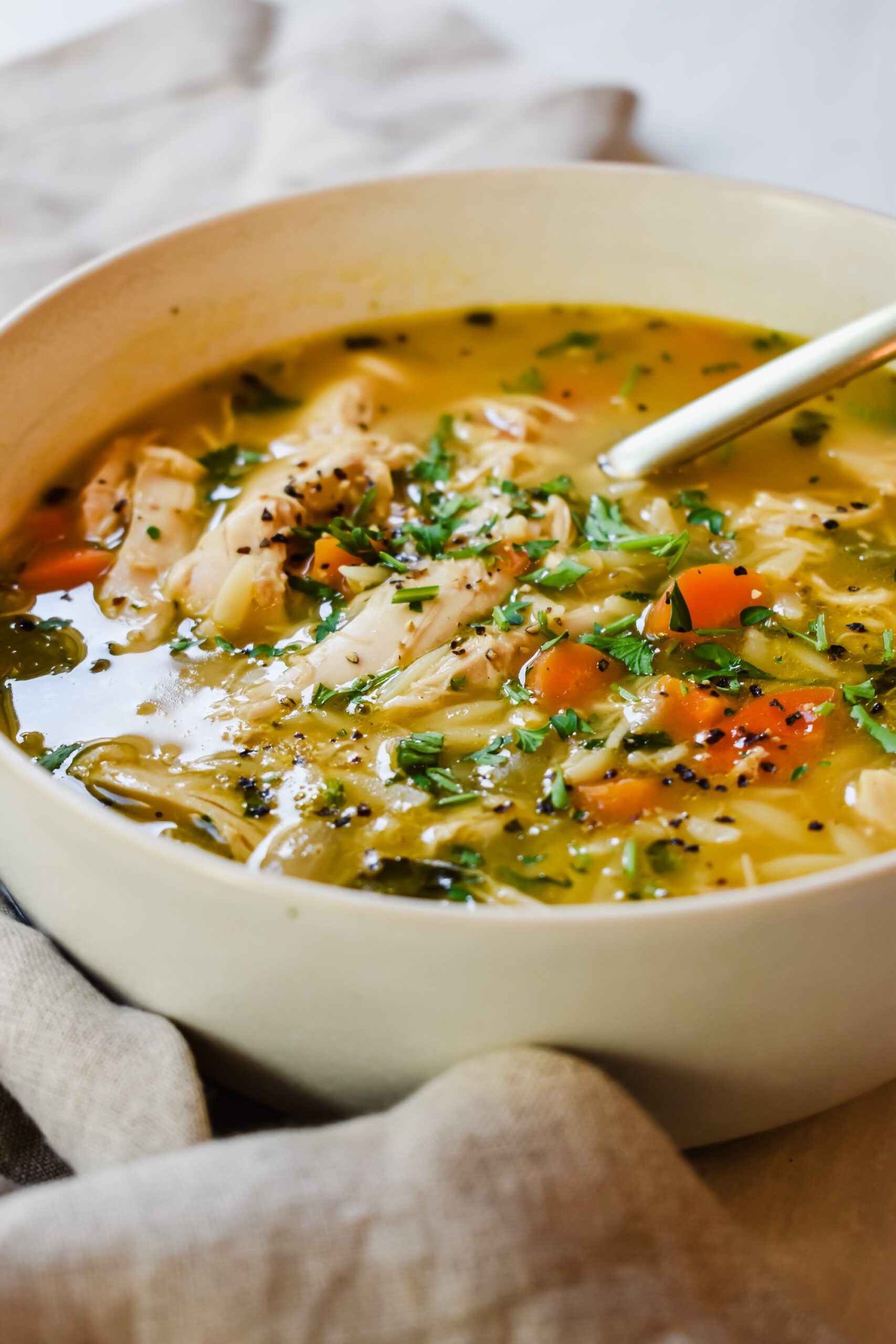 This is a side view close up of my greek chicken soup with lemon and orzo in a bowl with a golden spoon. 
