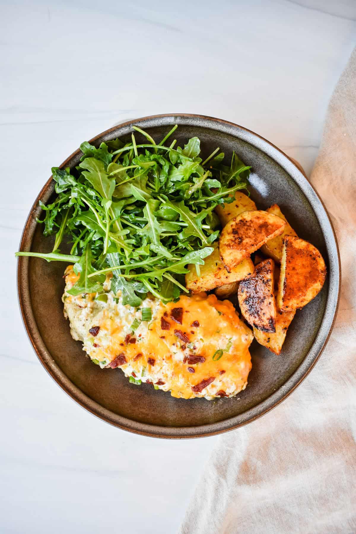 this is a top view of my chicken bake on a plate with the potatoes and arugula. 