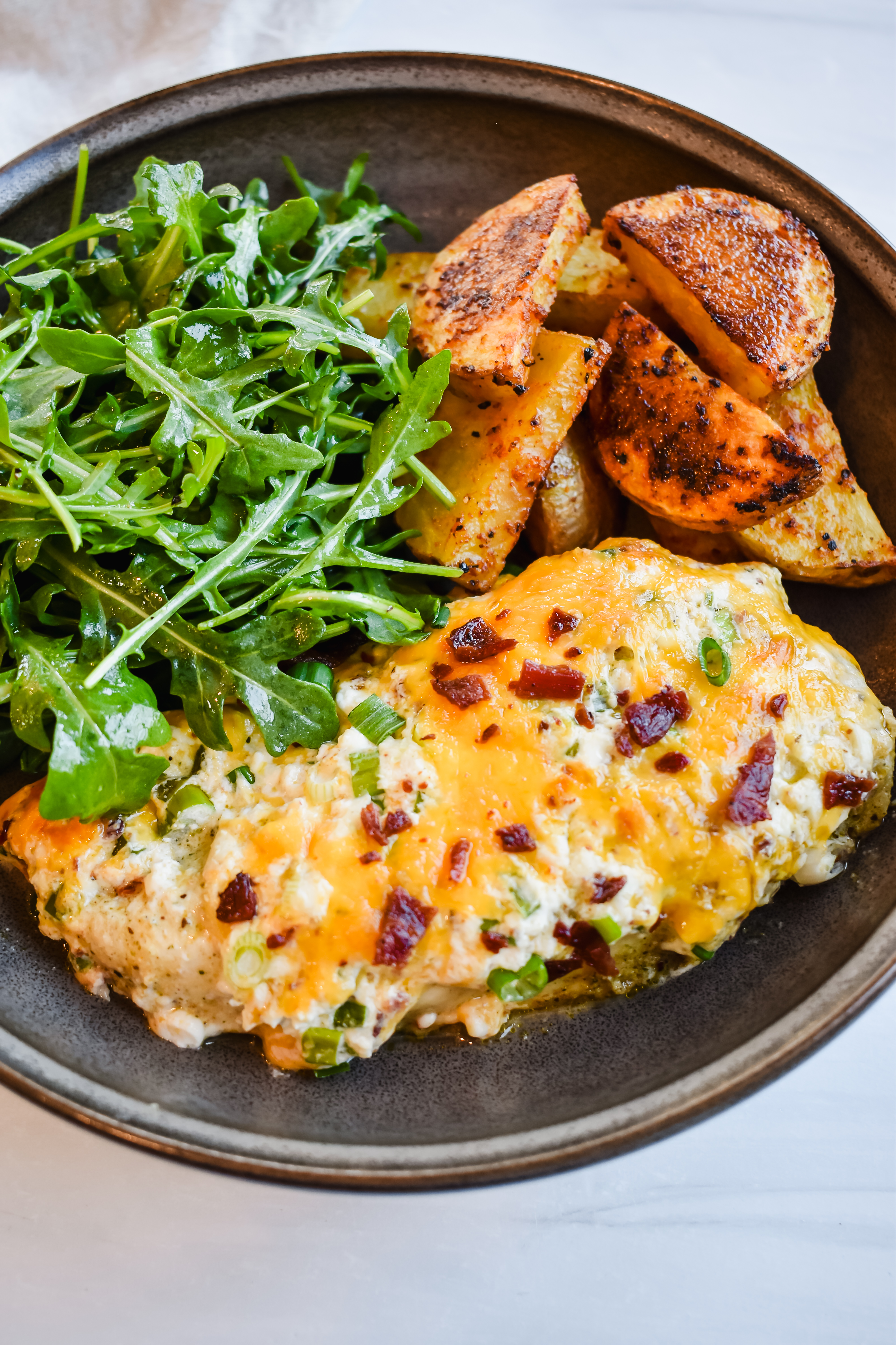 this is a side view close up of my healthy million dollar chicken bake served on a plate with roasted potatoes and a simple arugula salad. 
