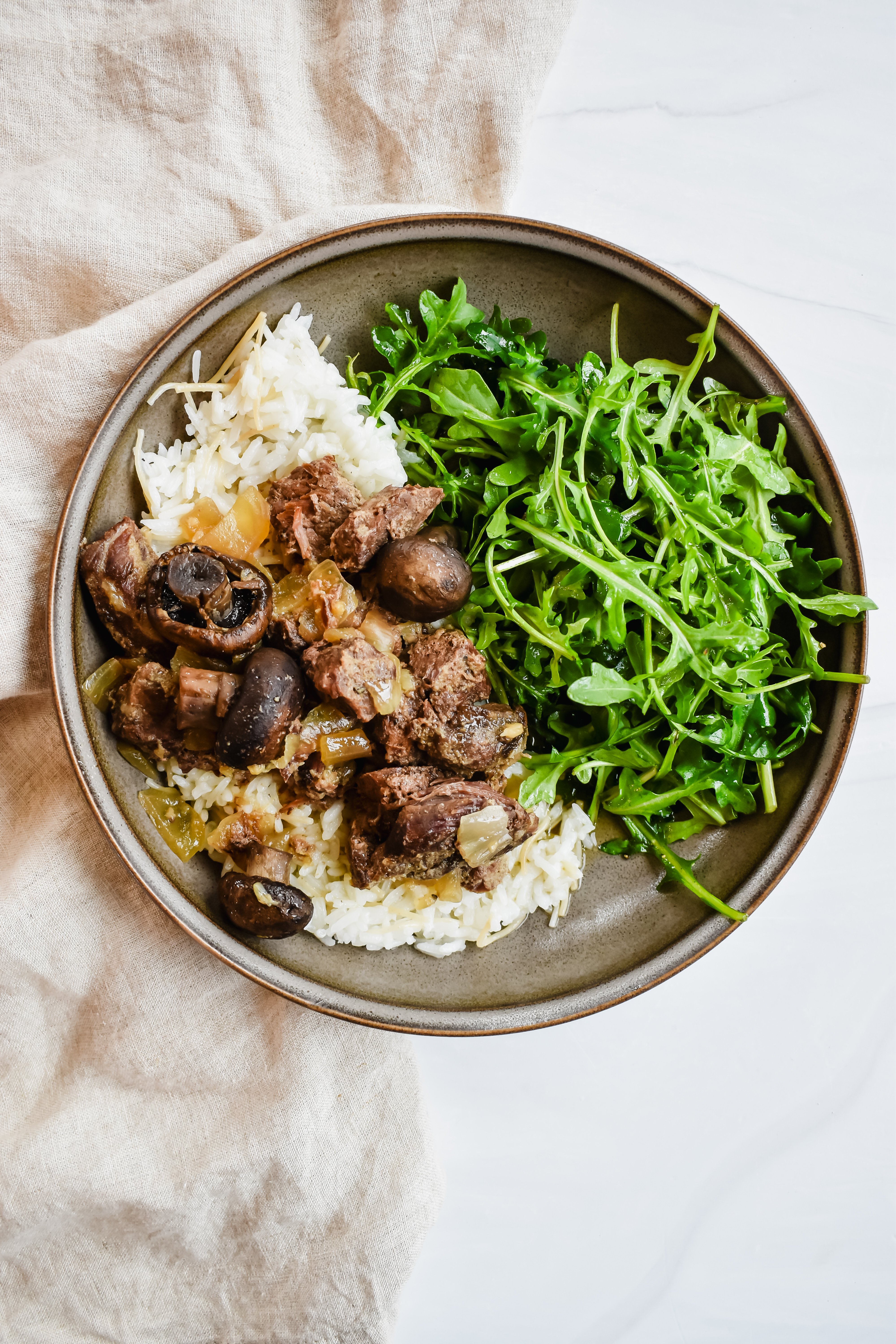 top view close up of my crockpot garlic butter steak bites on top of rice and served with an arugula salad. 