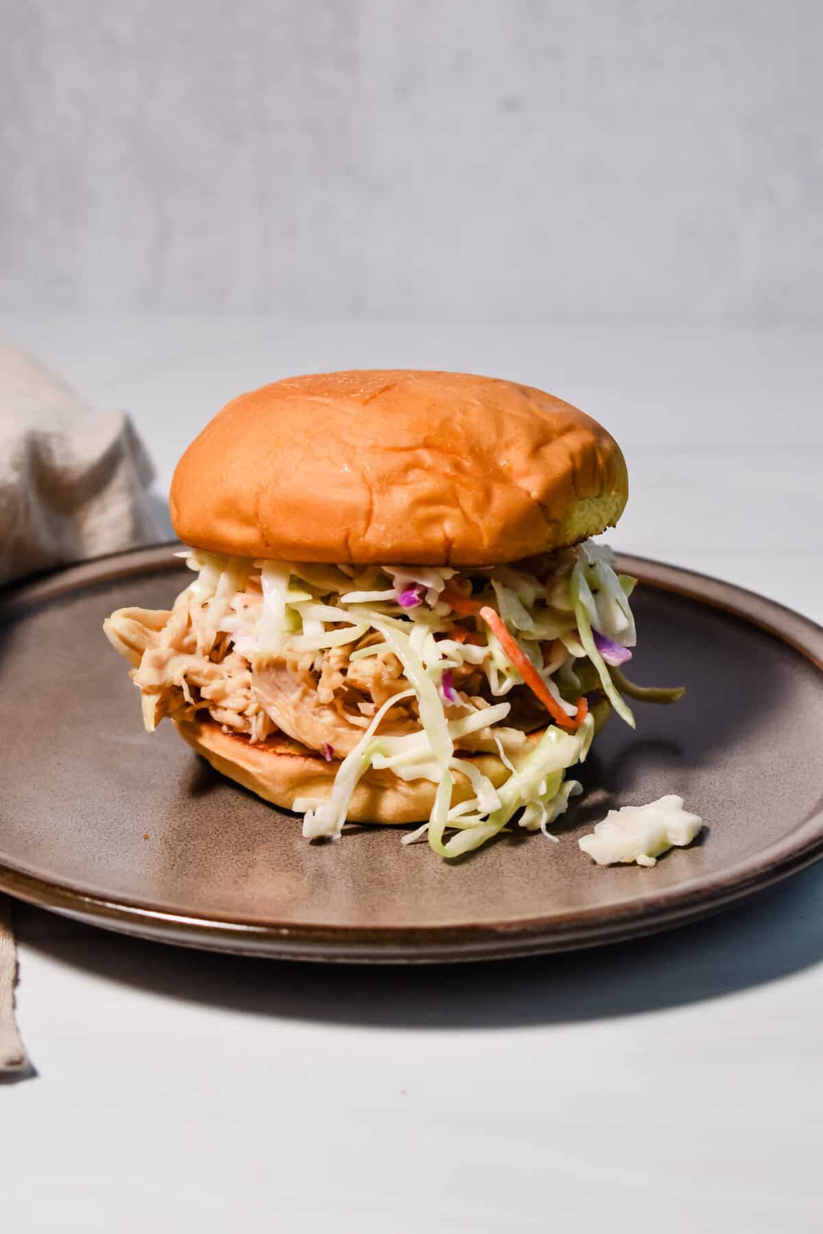 this is a photo of my slow cooker honey mustard chicken in a sandwich with some coleslaw on a plate. 