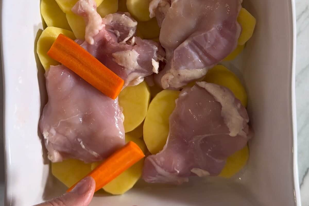 this shows the potatoes, carrots and chicken thighs in a baking pan.