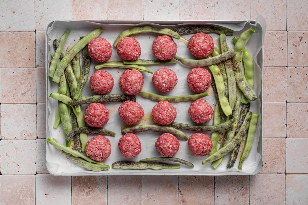 Overhead shot of meatballs formed on sheet pan with green beans.