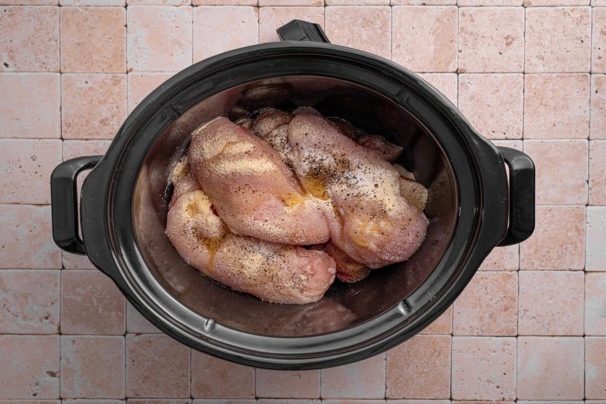 Overhead shot of chicken and seasonings in slow cooker.