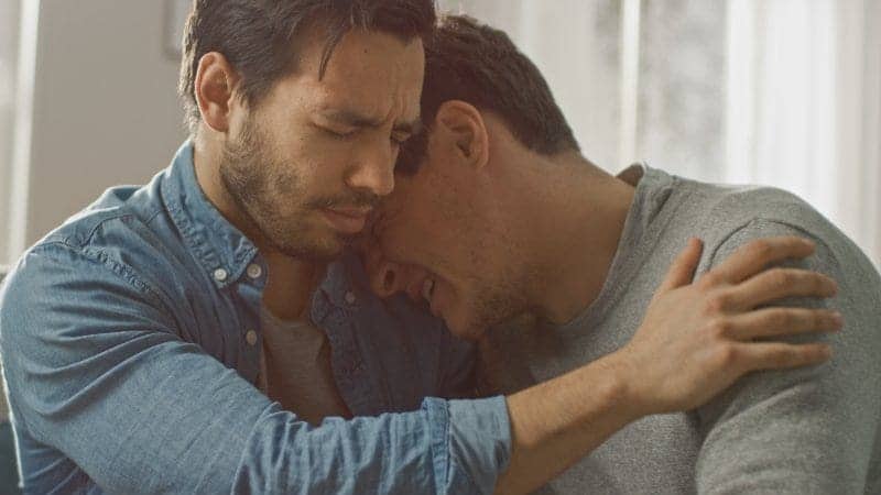 A man comforts another man in tears leaning on his shoulder
