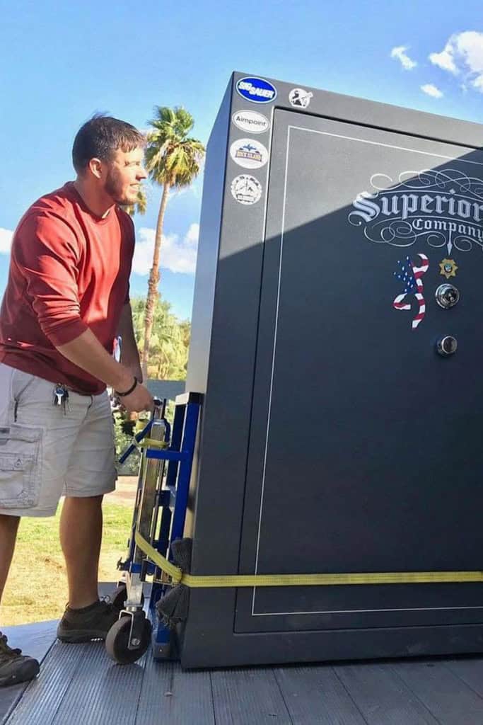 Man in a red shirt moving a large black safe on a hand truck outdoors