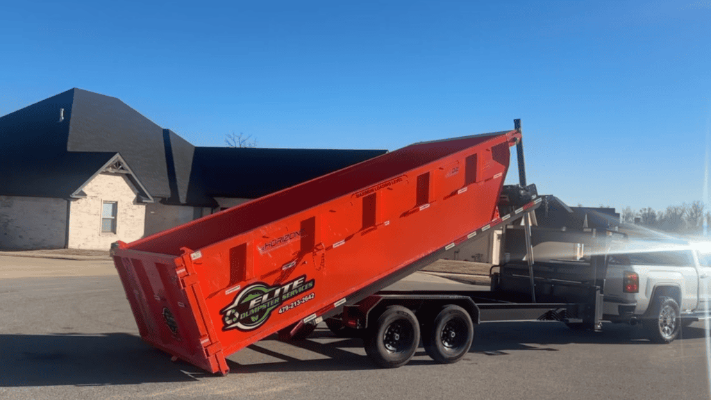 Red dumpster being unloaded from truck for waste disposal.