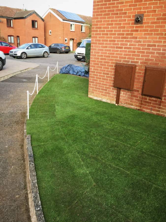 Lush green garden lawn with edging and nearby parked cars.