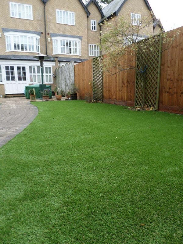 Lush artificial grass lawn in Suffolk with wooden fencing and residential buildings.