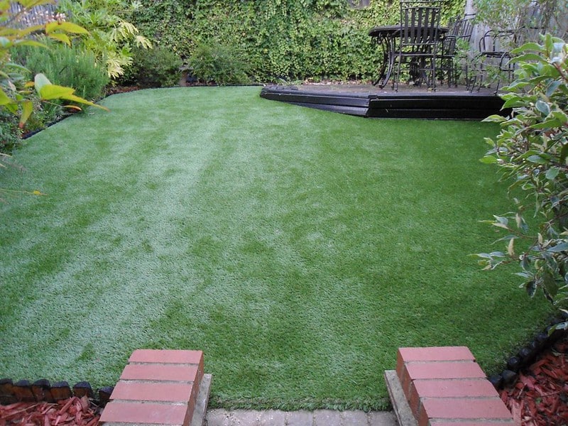 Artificial grass lawn in a garden with seating area and surrounding plants.