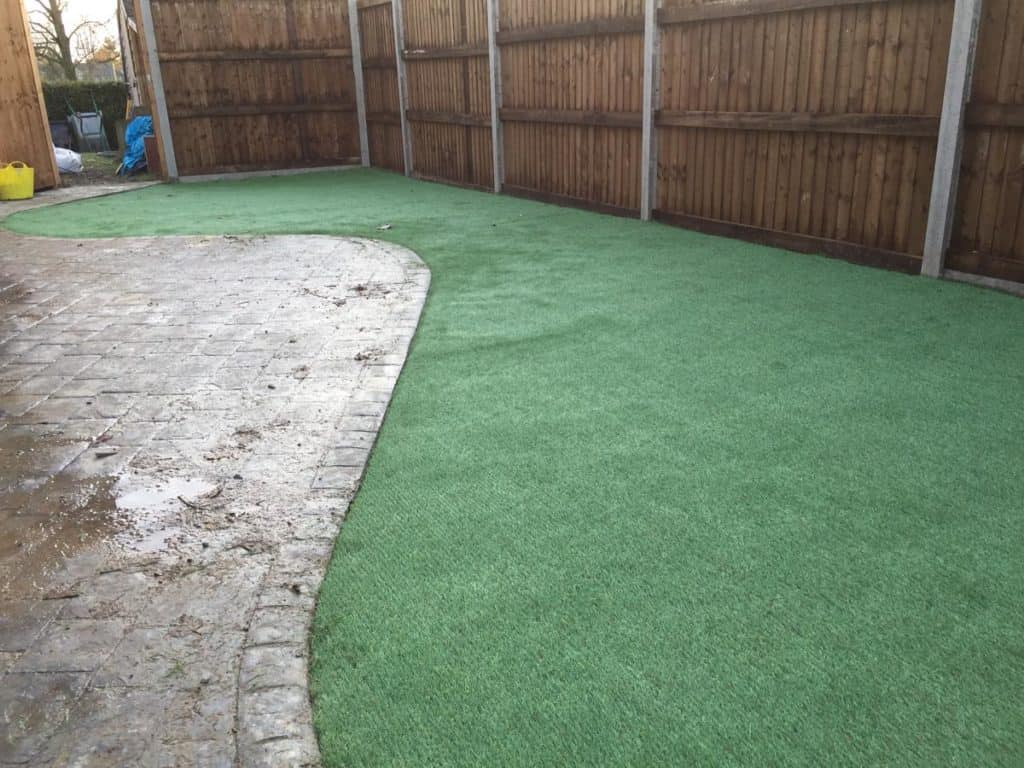 Artificial grass garden with curved design and wooden fence.