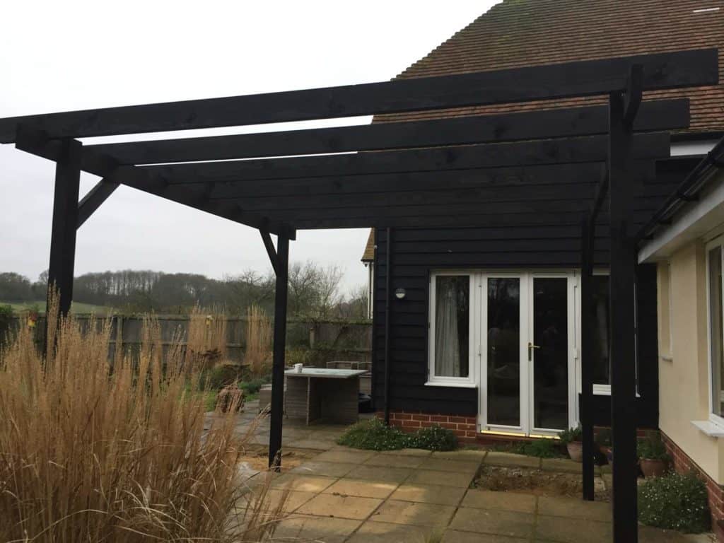 Black wooden pergola attached to house in Suffolk garden.
