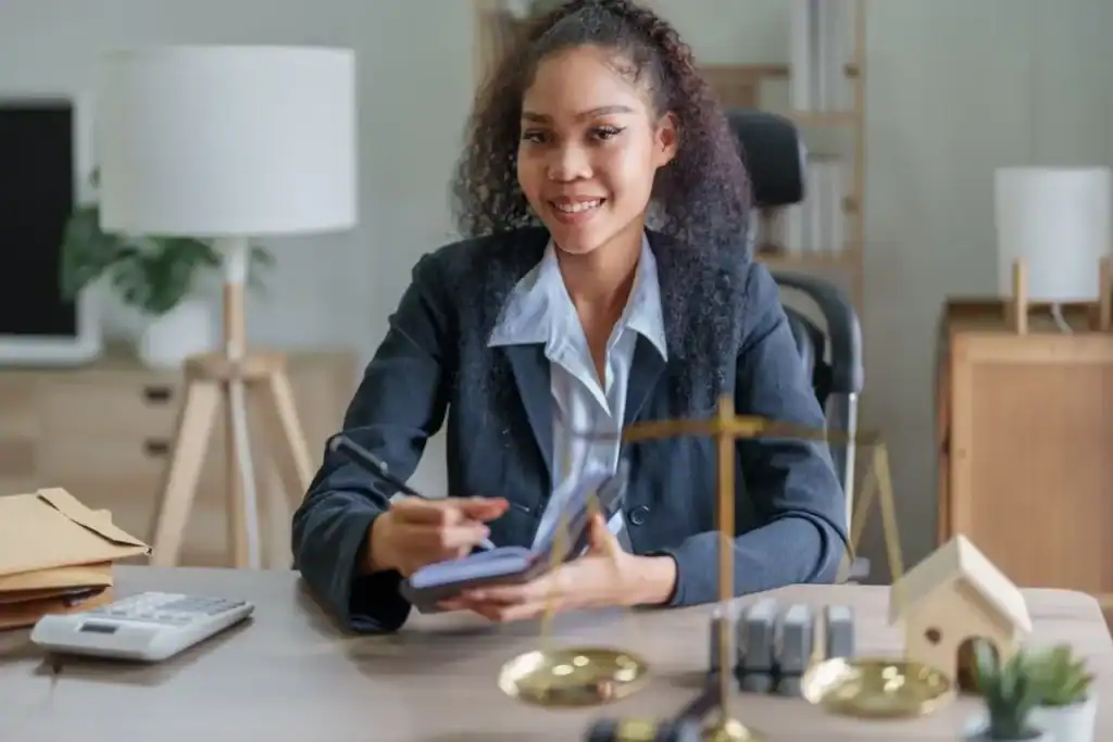 Young woman smiling at desk with office supplies and house model.