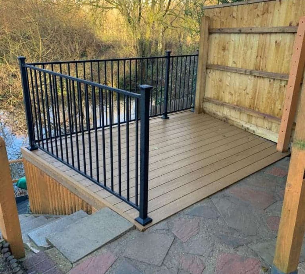 Durable composite decking with black metal railing in garden setting.