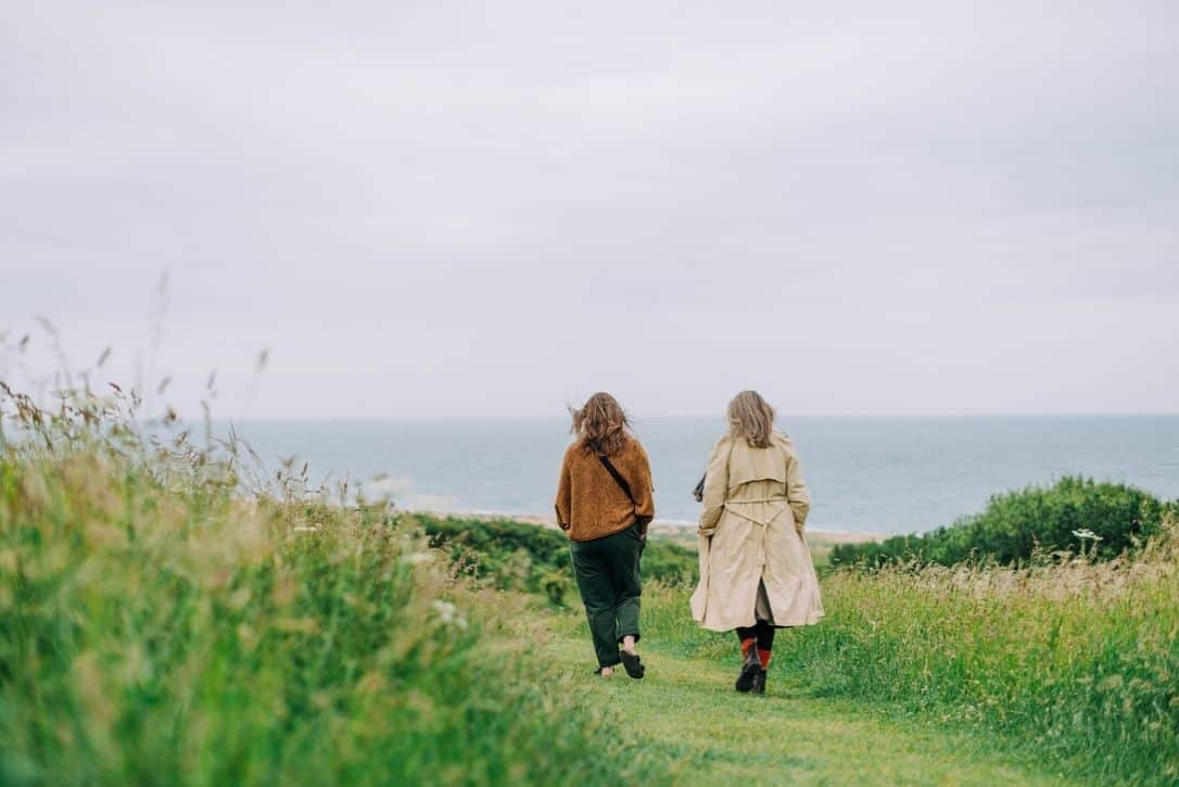 Photo of two figures walking along a path towards the sea