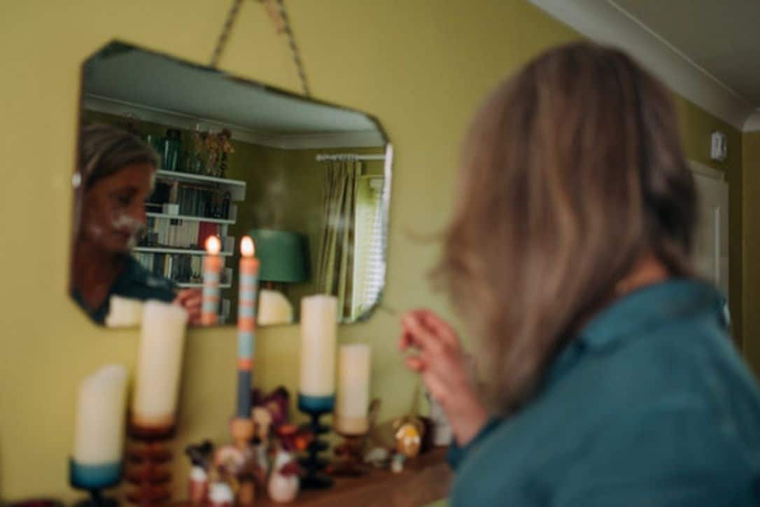 Photo of Emma reflecting in a mirror as she lights candles.