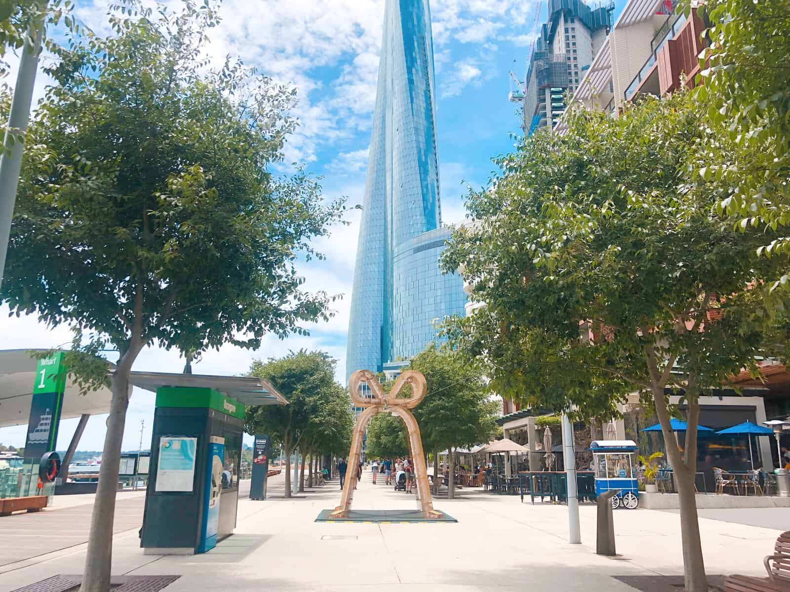 A skycraper stands in the background. In the foreground is an archway in the shape of a bell covered in lights.