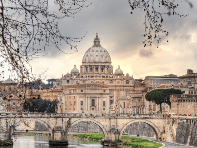 Vatican City skyline with St. Peter's Basilica dome in the background, framed by tree branches, showcasing the historic architecture and scenic beauty of the Vatican.