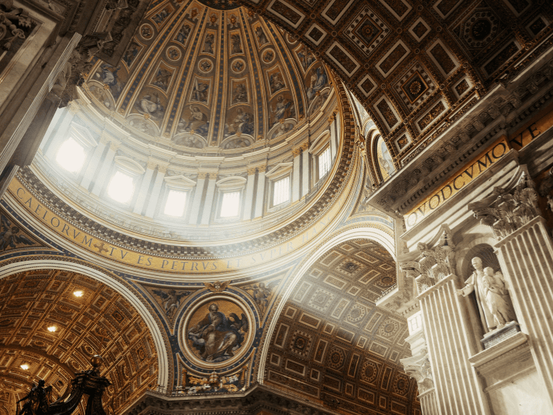 Vatican Dome ceiling with intricate gold detailing and natural light streaming through windows, showcasing the grandeur of the sacred space.