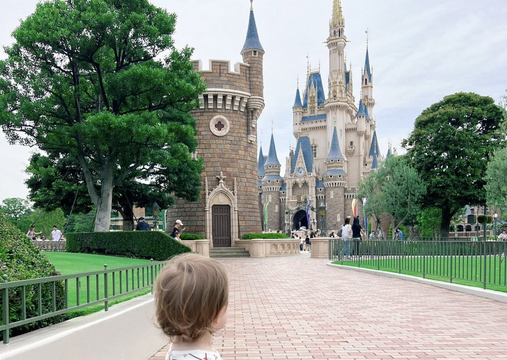 A young child gazes at the iconic Cinderella Castle at Tokyo Disney, surrounded by lush greenery and a clear sky, capturing the magic of a family-friendly Disney adventure.