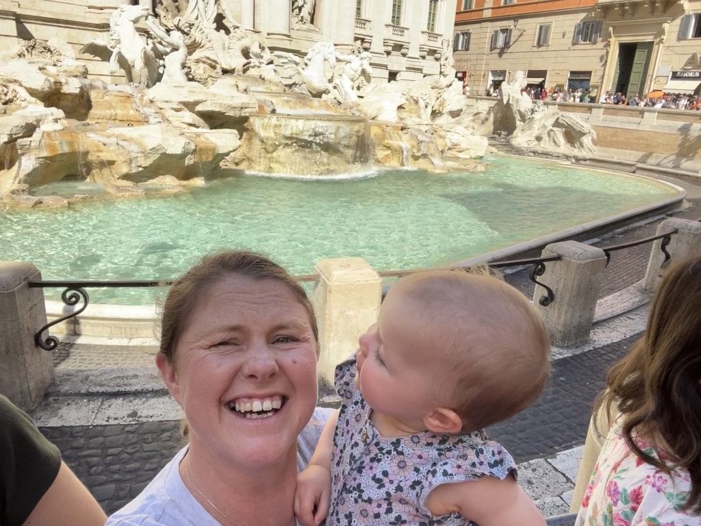 A joyful mother and her baby exploring Rome’s iconic Trevi Fountain, capturing a memorable family moment amidst historic architecture and lively city atmosphere.