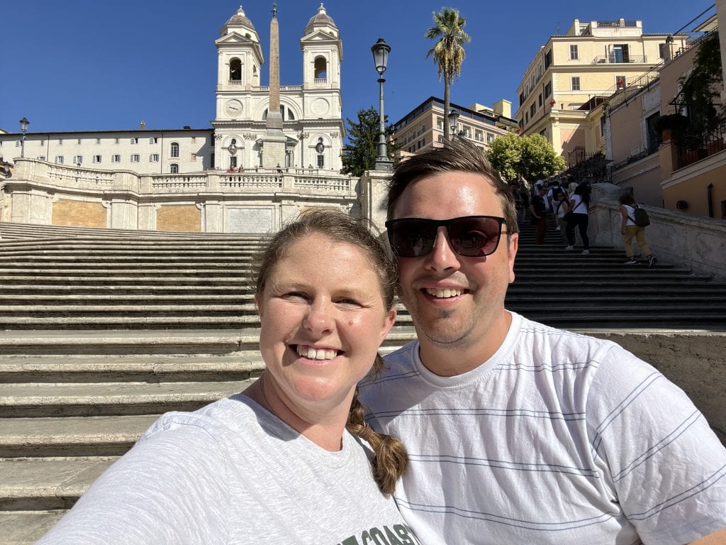 Happy family exploring Rome with a baby, sitting on historic steps near the church, enjoying sunny weather and city views. Perfect for family-friendly travel tips in Rome.