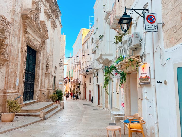 Charming narrow street in Lecce, Italy, with historic architecture, vibrant outdoor cafes, and bright blue sky, showcasing Italian culture and Mediterranean atmosphere.