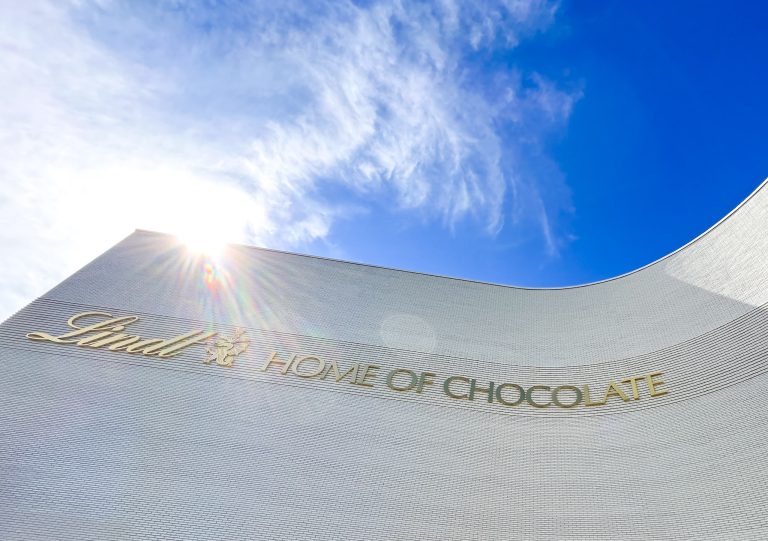 Lindt Home of Chocolate building with sunlight and blue sky, showcasing the iconic sign at the entrance. Perfect for chocolate lovers and families exploring the sweet destination.