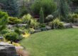 Well-manicured backyard garden with stone borders, evergreen shrubs, and a green lawn