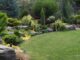 Well-manicured backyard garden with stone borders, evergreen shrubs, and a green lawn