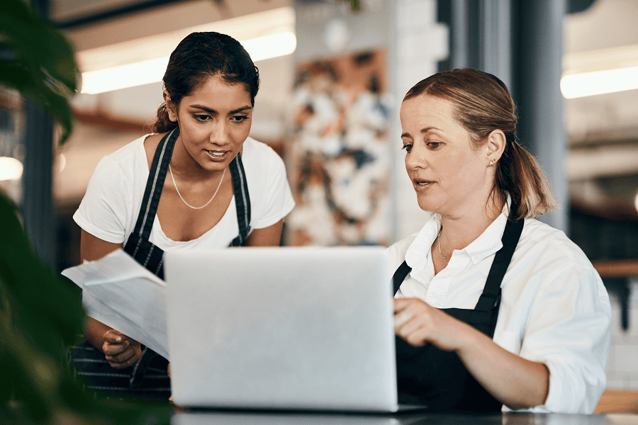 Two women discussing customer feedback on a laptop in a cafe setting.