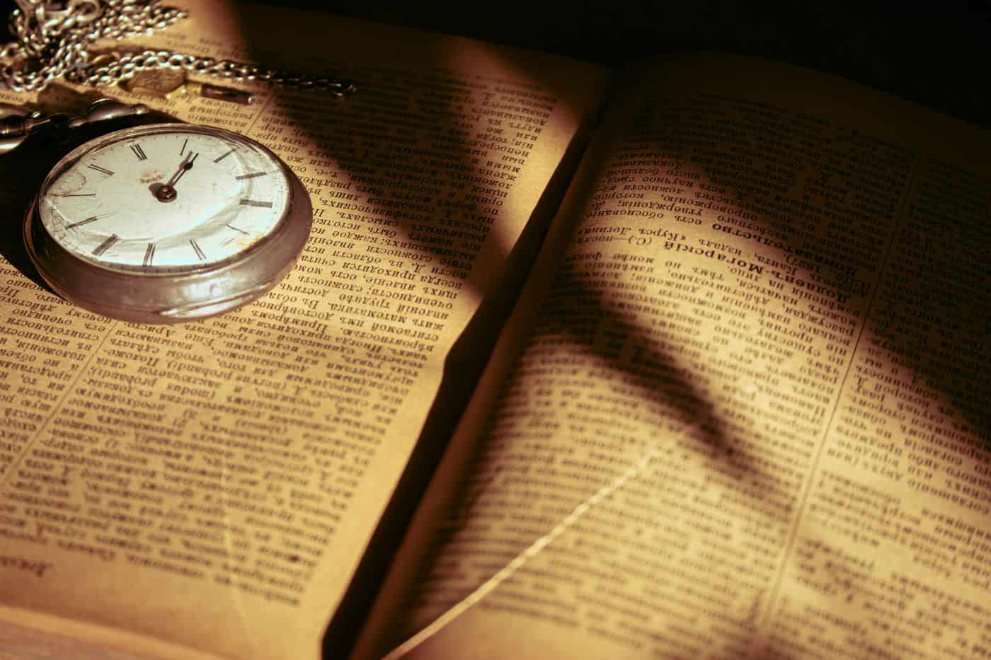 Reloj antiguo sobre libro abierto con sombra de reloj, en ambiente sombrío y reflexivo.
