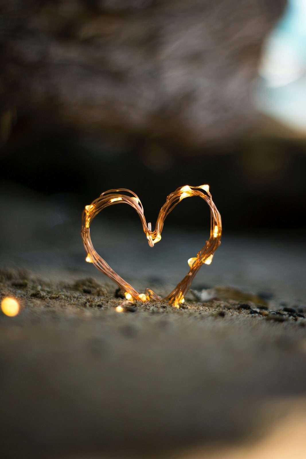 Corazón de luces de hilo en la arena, simbolizando amor y filosofía en la penumbra.